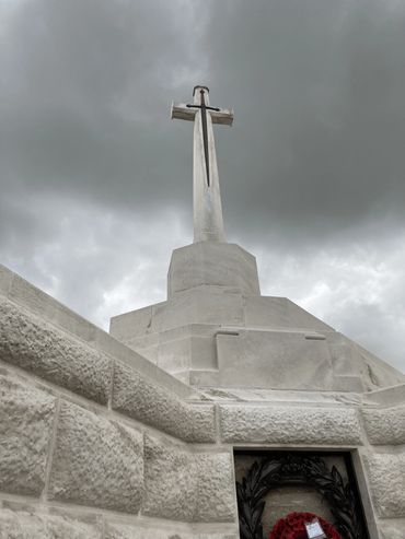 A raised marble cross at a war memorial bearing a metal sword against a dark, overcast sky.