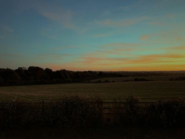 Large open fields on a hillside in front of a blue and orange sunset sky.
