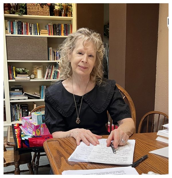 Woman with curly hair working on handwritten notes at a wooden table.