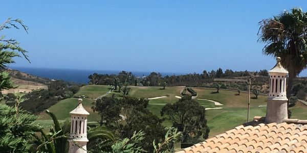Scenic view of a golf course with ocean in the background and rooftops in the foreground.