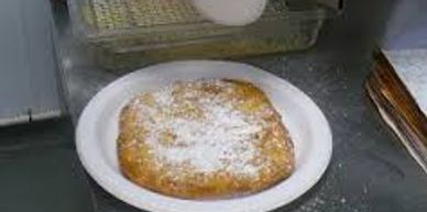 A fried pastry dusted with powdered sugar on a white plate.