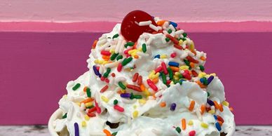 Whipped cream dessert topped with colorful sprinkles and a red cherry.