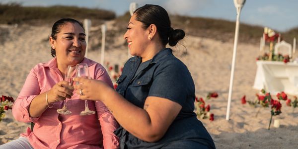 Two women clinking glasses on the beach.