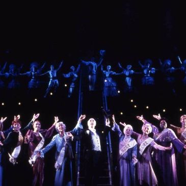Group of performers in vintage attire on stage with raised arms.