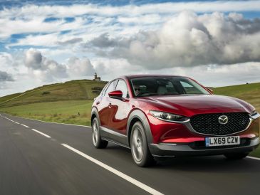 Red Mazda car driving on countryside road.