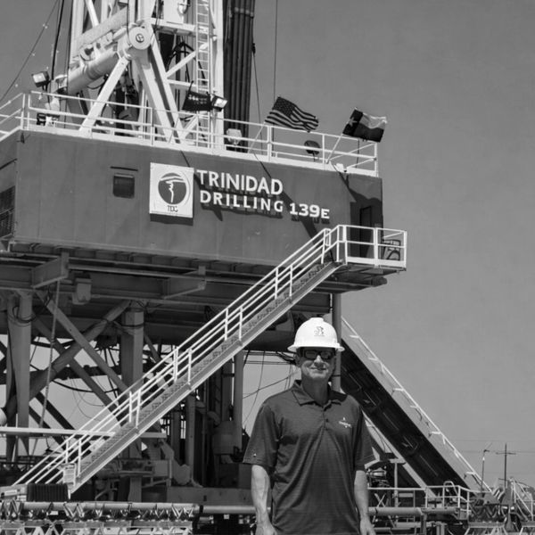 Man in hard hat stands in front of Trinidad Drilling 139E rig.