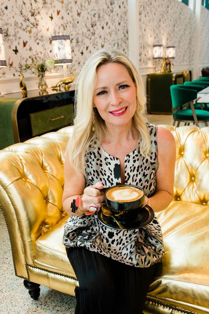 Denise Simons, smiling and holding a cappuccino.