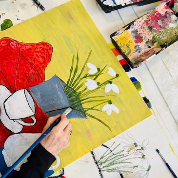 Artist painting white flowers in a gray vase on a yellow background.