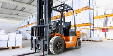 Orange forklift parked in a spacious warehouse with shelves.