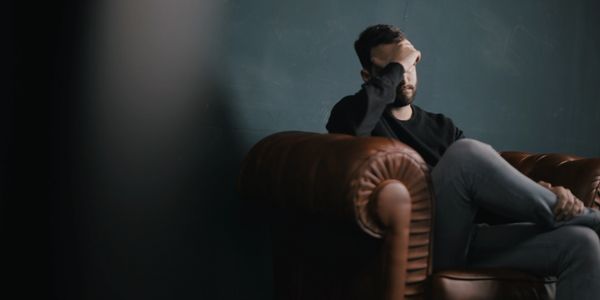 Traumatized man sitting on a brown couch with his head in his hand