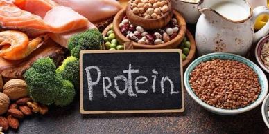 Various protein-rich foods surrounding a chalkboard with 'Protein' written on it.