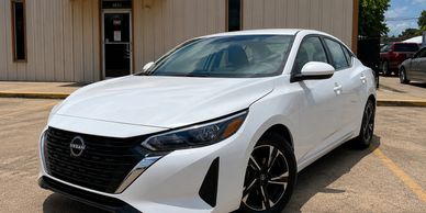 White Nissan sedan parked outside a building on a sunny day.