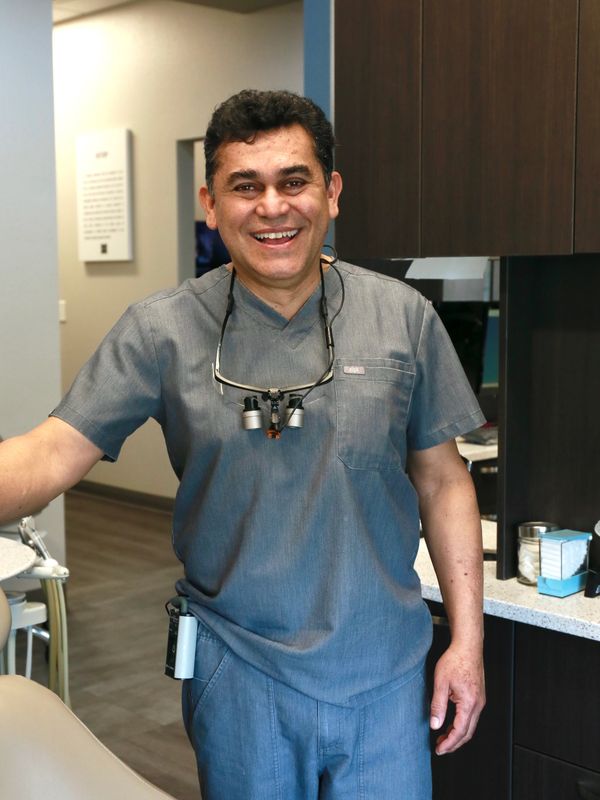 Smiling male dentist in scrubs with magnifying glasses around his neck.
