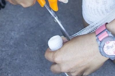 Hands cutting white mesh fabric with scissors on a gray surface.