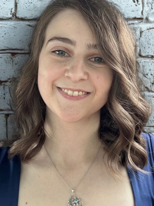 Young woman with curled hair smiling against a brick wall.
