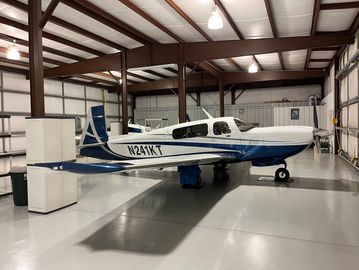 A white and blue small airplane inside a spacious hangar.
