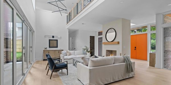 Modern living room with high ceilings and bright orange door.