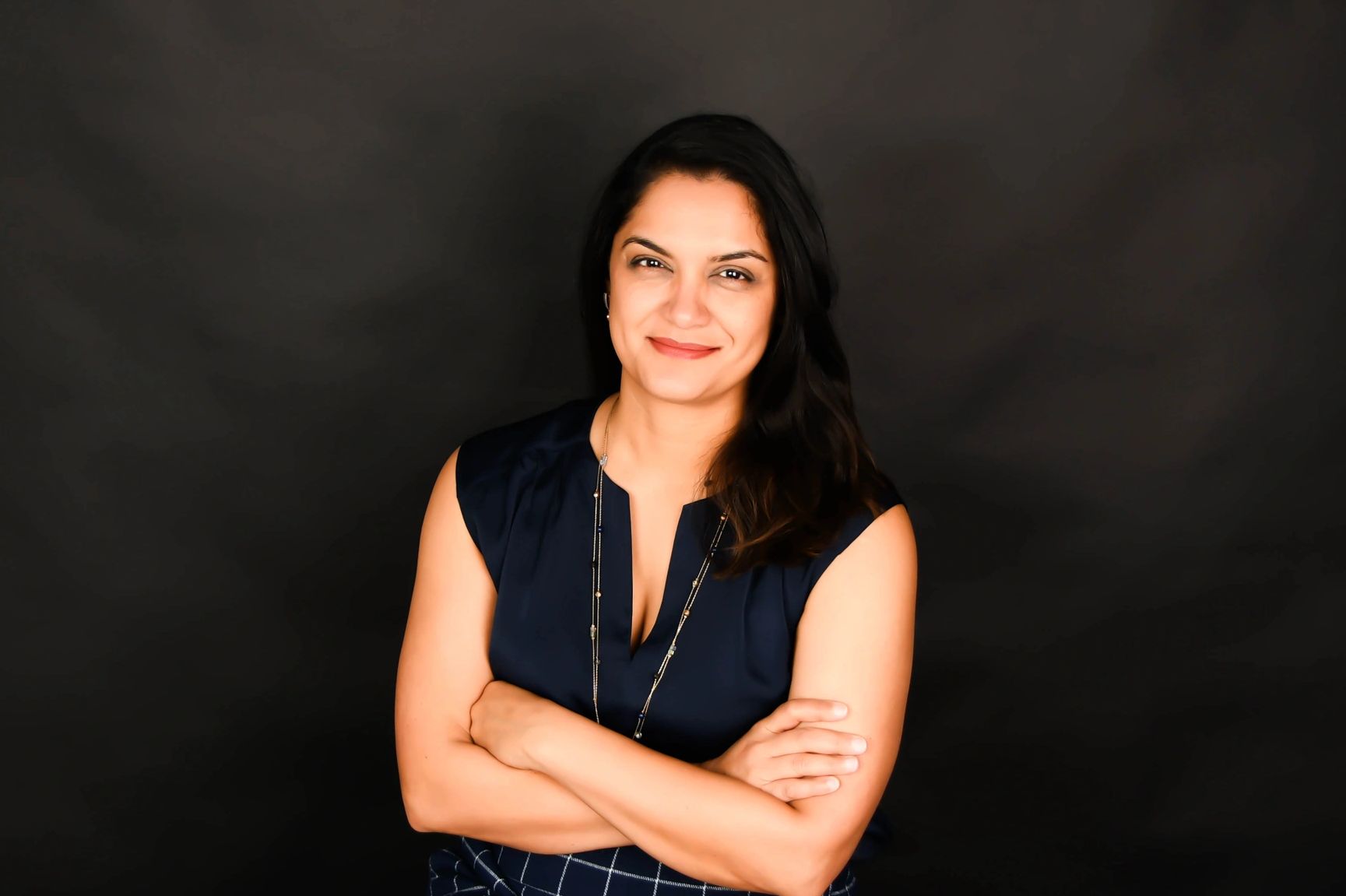 Confident woman with arms crossed, smiling against a dark background.