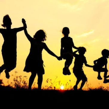 Silhouettes of children jumping and holding hands at sunset.