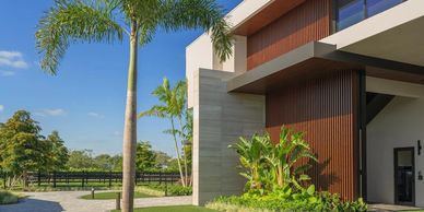 Modern house exterior with palm trees and landscaped lawn under a clear blue sky.