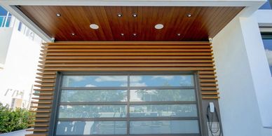 Modern garage door with wooden slats and glass panels under a wooden-paneled ceiling.