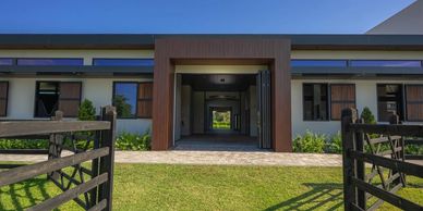 Modern stable entrance with wooden gates and lush green lawn under a clear blue sky.