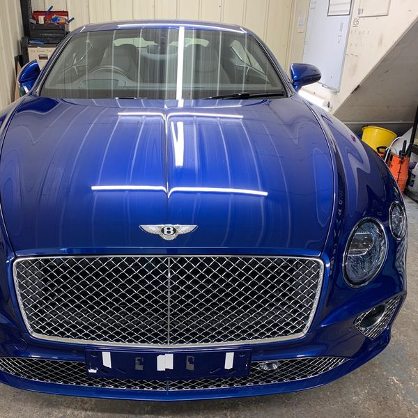 Front view of a shiny blue Bentley car in a garage.