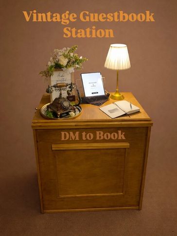 A vintage guestbook station with an antique phone, lamp, and open book on a wooden table.