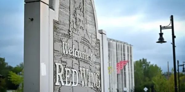 A weathered sign welcoming visitors to Red Wing against a cloudy sky.
