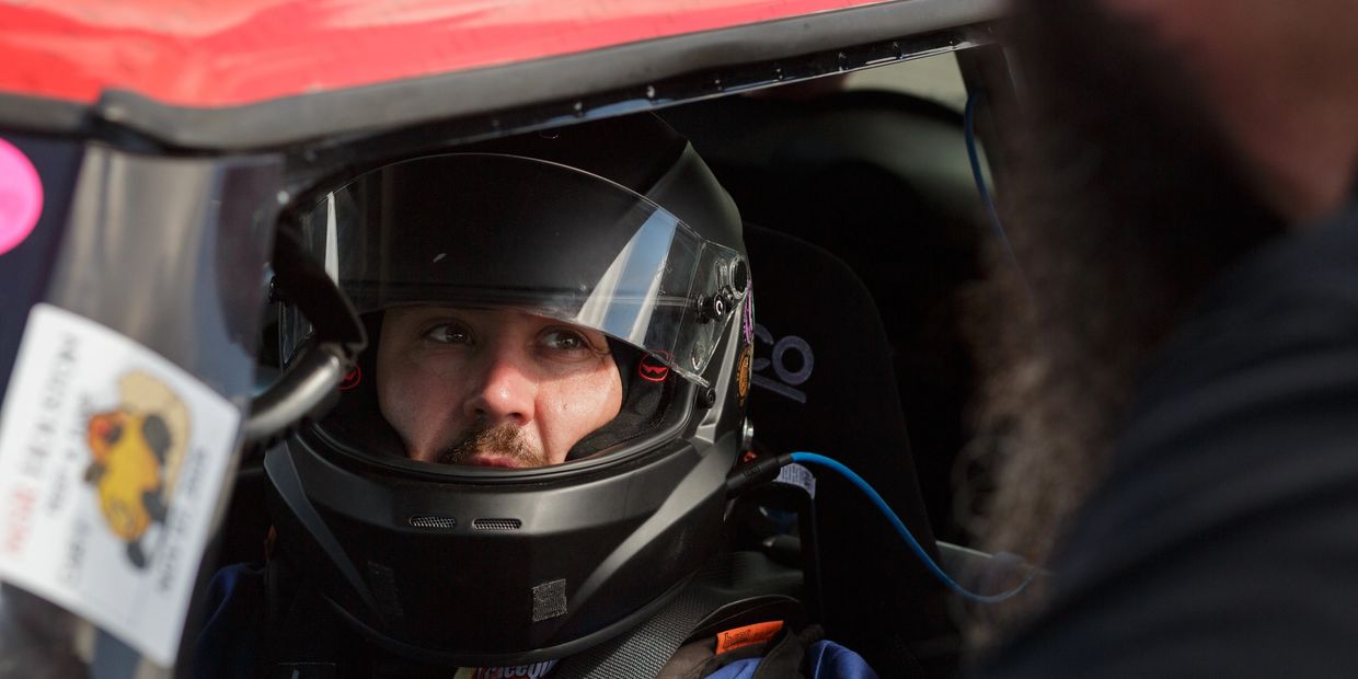 Race car driver in helmet inside a car.