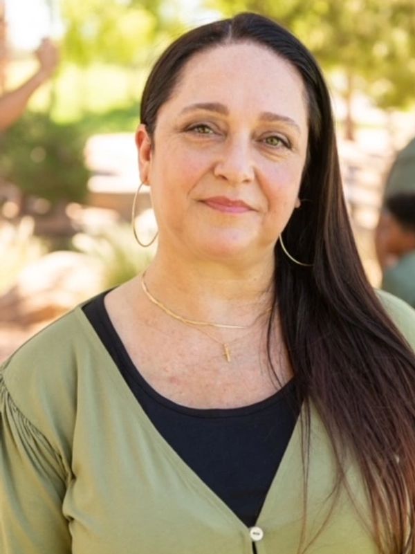 Woman with long dark hair wearing hoop earrings and a green top outdoors.