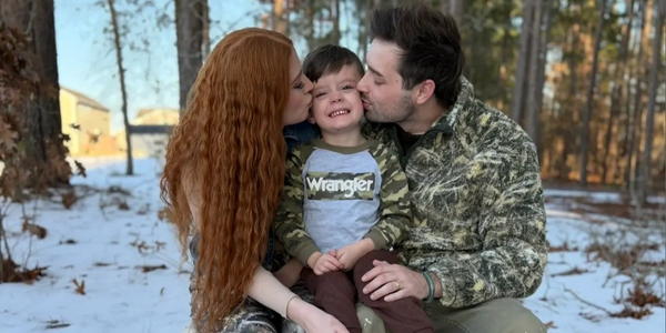 Parents kissing their happy child outdoors in a snowy forest.