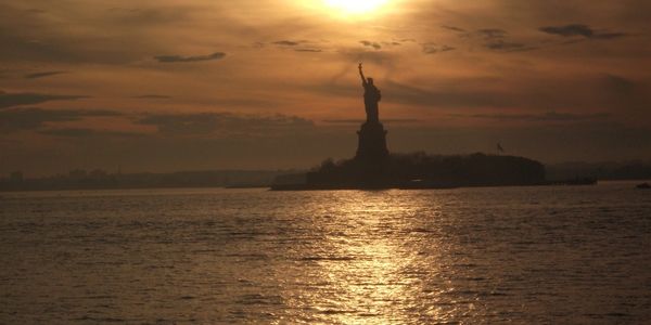 Silhouette of the Statue of Liberty at sunset over water.