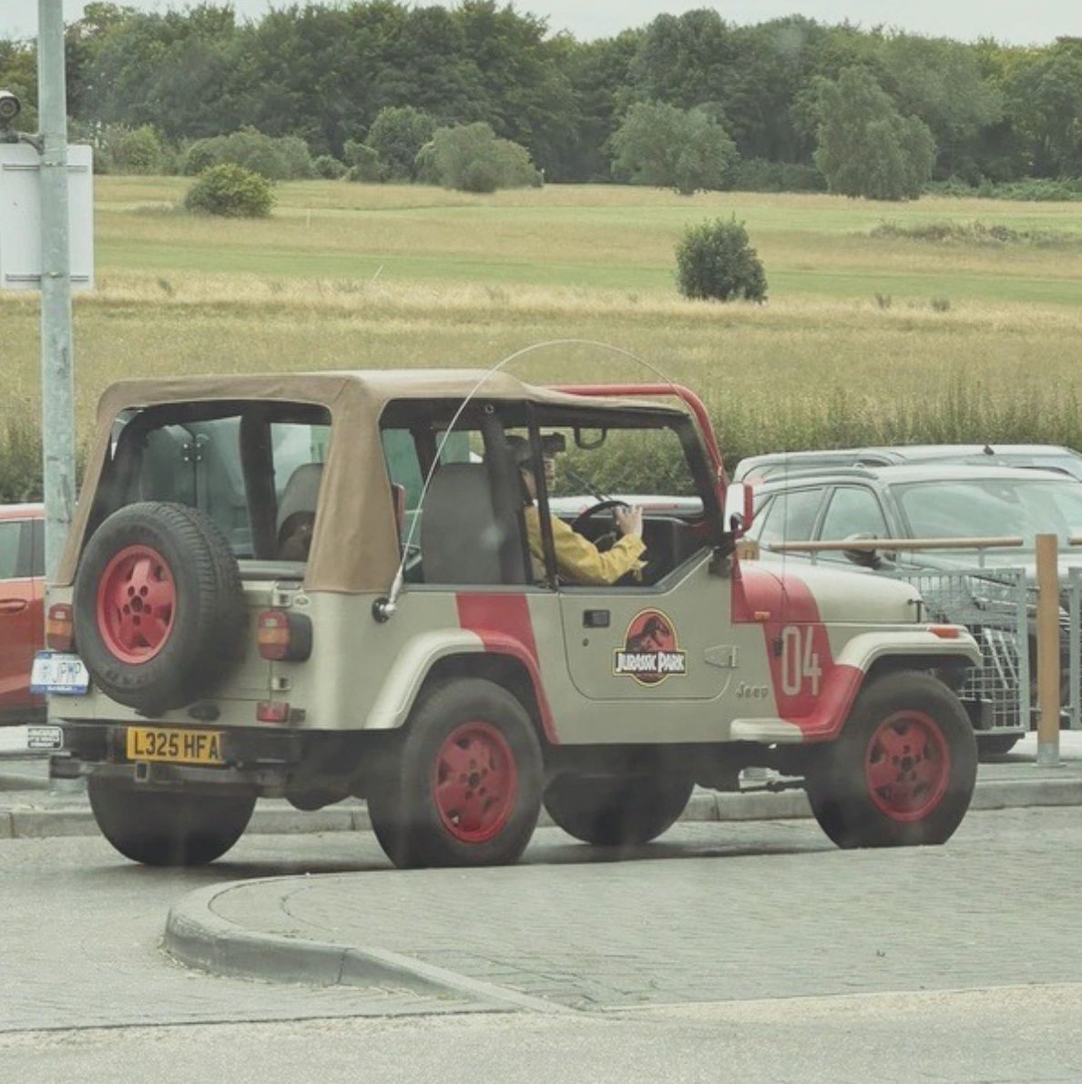 JP04 Jurassic Park Jeep driving through car park near grassy fields