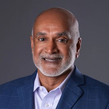 Smiling man in a blue suit jacket and white shirt against a gray background.