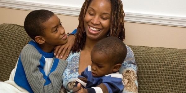 Mother with two young sons smiling on a couch.