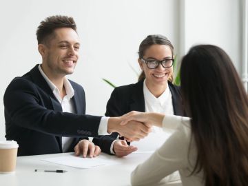 Two professionals shaking hands with a woman during a meeting.