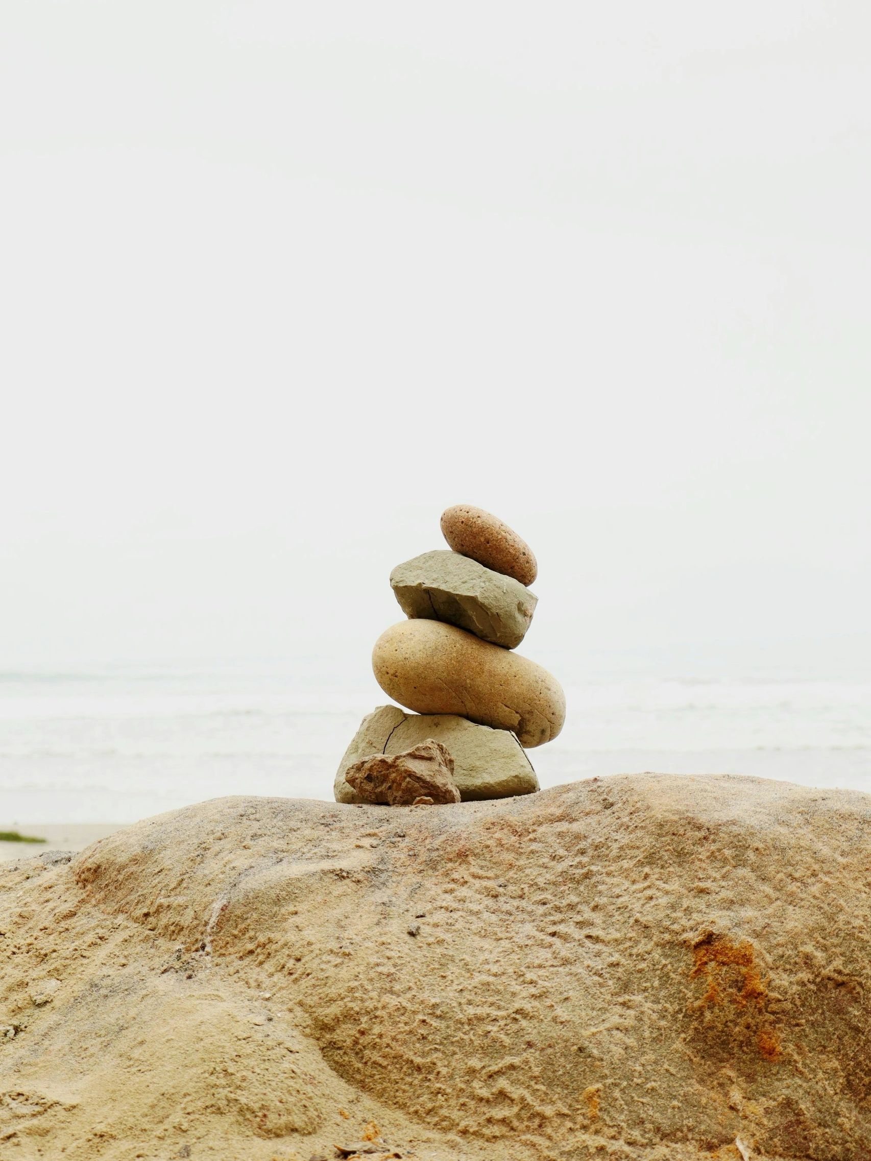 A small stack of balanced stones on a sandy surface by the sea.