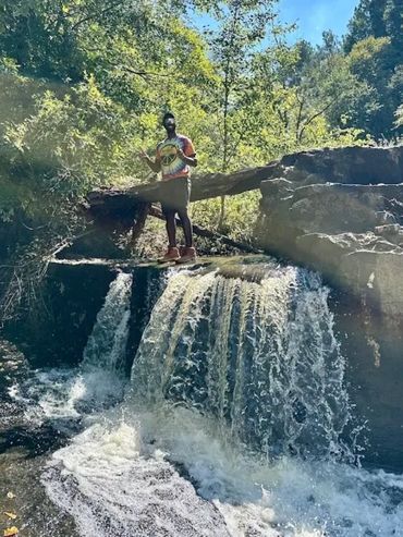 Man with a bright shirt standing on top of a rushing waterfall. 