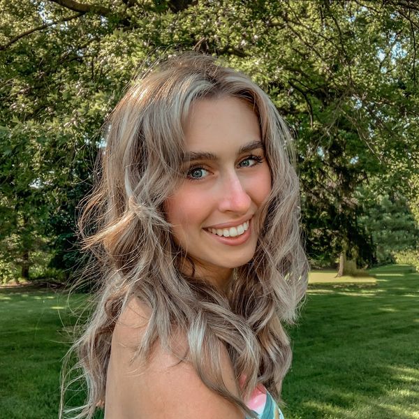 Young woman smiling outdoors with wavy blonde hair and green eyes.