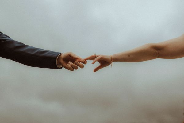 Two hands reaching out to touch against a cloudy sky.