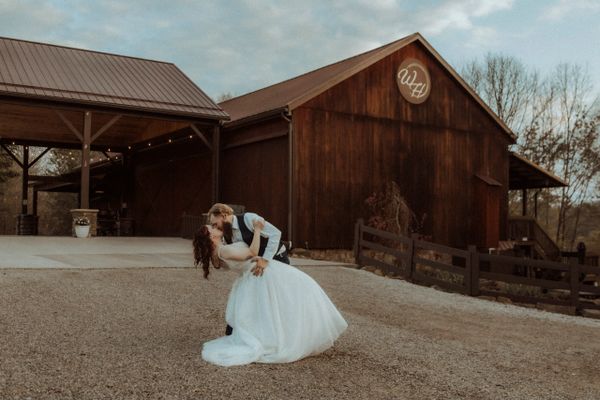 Bride and groom share a romantic dance outside a rustic barn.