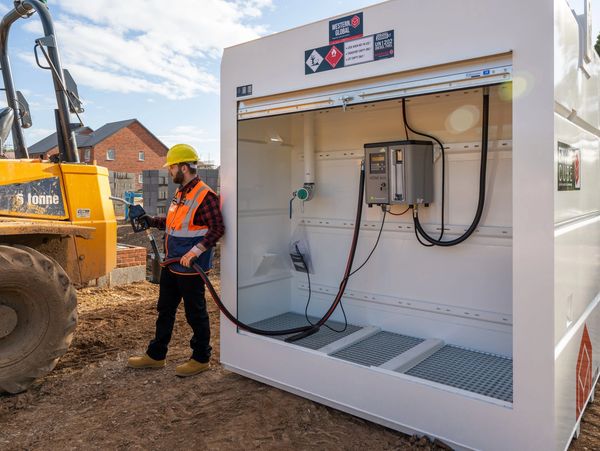 Construction worker refueling heavy machinery at a site fuel station.