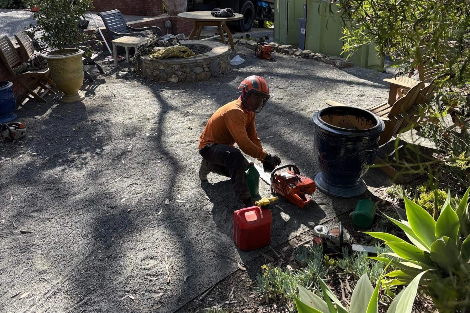 Peterson's Tree Works crew member in helmet, face shield and gloves fueling a chainsaw for tree work