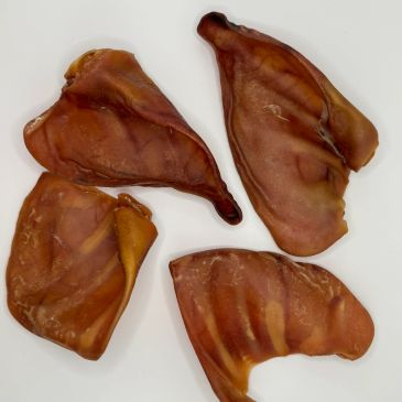 Four dried pig ears on a white surface.
