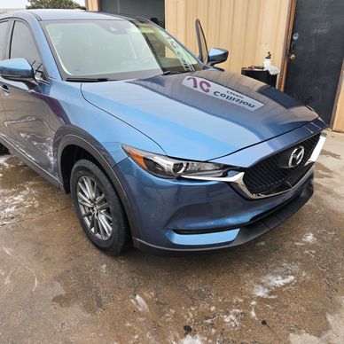 Blue Mazda SUV parked near a building with the driver's door open.