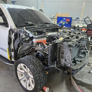 A white vehicle with its front end dismantled in a workshop.