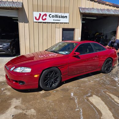 Red sports car parked outside JC Collision Center on a sunny day.
