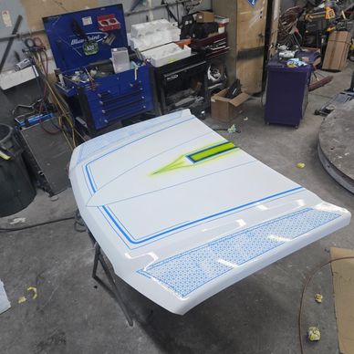 A freshly painted car hood with blue and green detailing in a workshop.