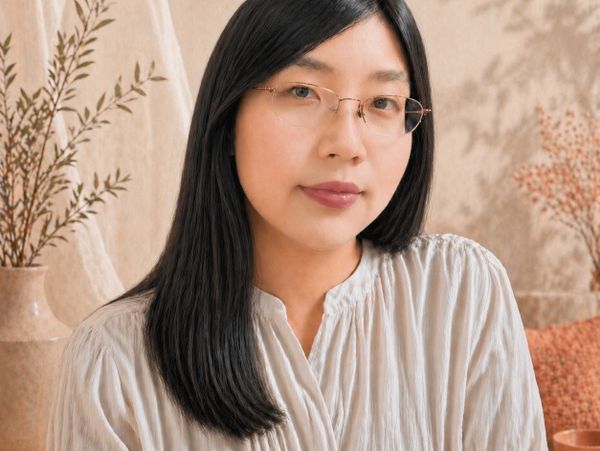Portrait of a woman with glasses and long black hair in a soft-toned setting.